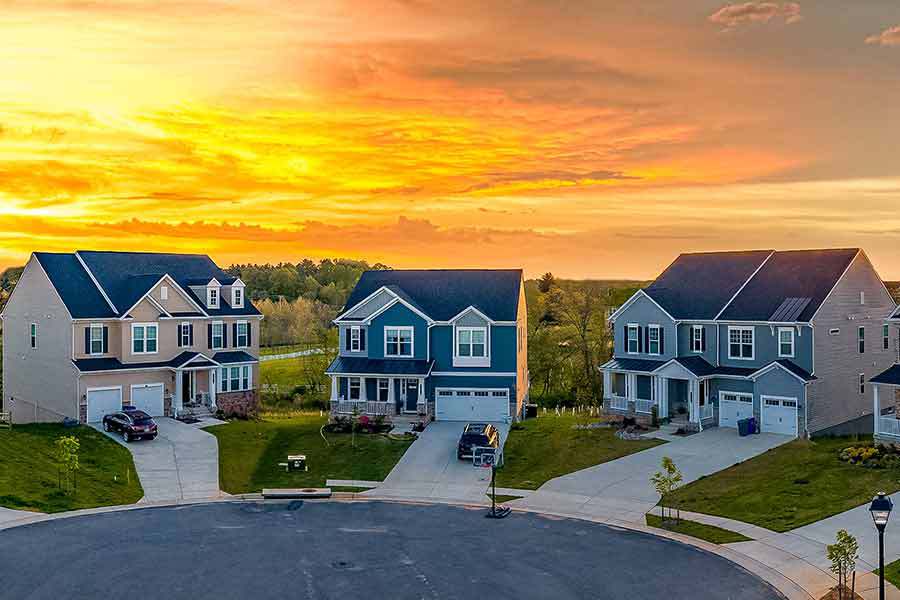 Three houses in a homeowner association community center with cars in the driveway and a sunset behind showcasing a nicely kept HOA community.