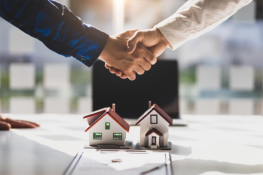 Property managers of a property management company shaking hands with a tenant with two houses beneath them.